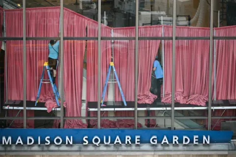AFP via Getty Images Workers are pictured through glass hanging curtains inside the venue above a sign reading 'Madison Square Garden' on Friday.