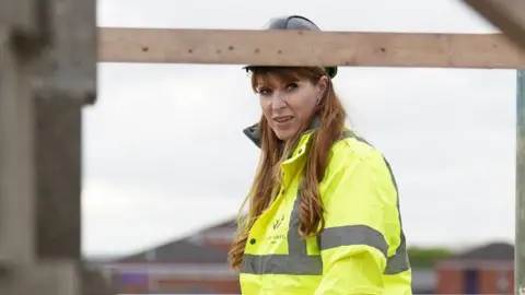 Angela Rayner pictured at a building site wearing a yellow hi-vis jacket and a black hard hat