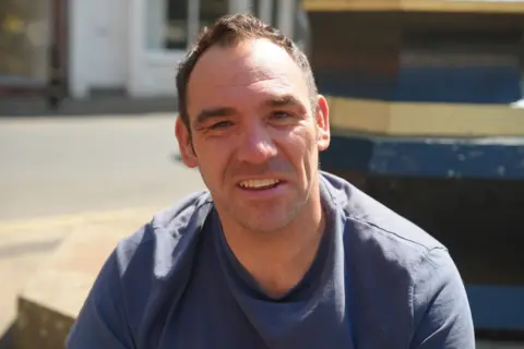 Sarah-May Buccieri/BBC Rob Heywood pictured in Louth. He is wearing blue top and has short dark hair. There are shopfronts in the background.