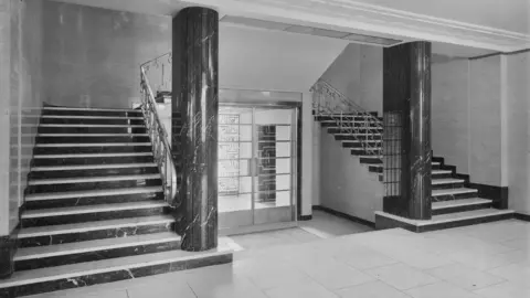 Historic England Archive A black and white image of the interior of the building, featuring a double staircase.