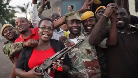 AFP Zimbabweans celebrate with soldiers on the street including a woman in a red T-shirt and black cardigan holding a machine gun in 2017