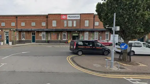 A generic image of Nuneaton station showing a taxi and other vehicles in front of a building. The two-storey building includes the word Nuneaton and the British Rail sign.