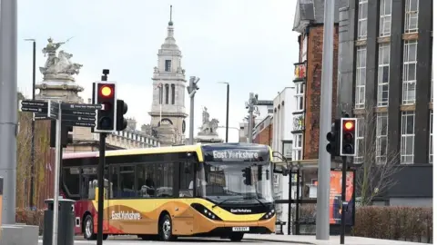 An East Yorkshire single-decker bus stops at traffic lights in Hull city centre. It has a orange, yellow and red livery 