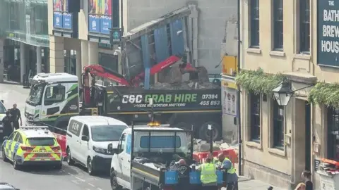 BANES Council A lorry has crashed into a wall. There are police cars parked nearby.
