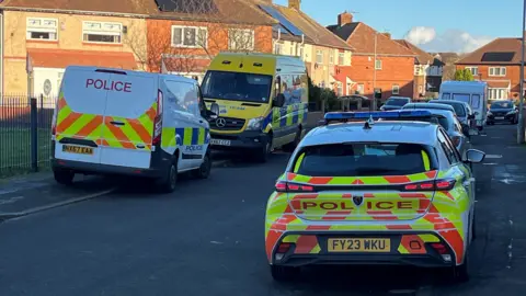 Police vans and cars parked in a residential street. 