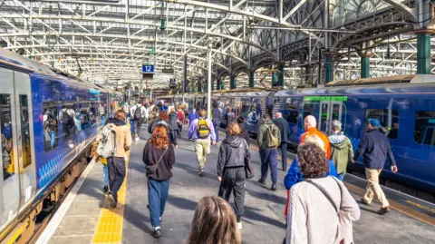 Getty Images Two blue ScotRail trains on either side of a platform. Passengers are walking along the platform.