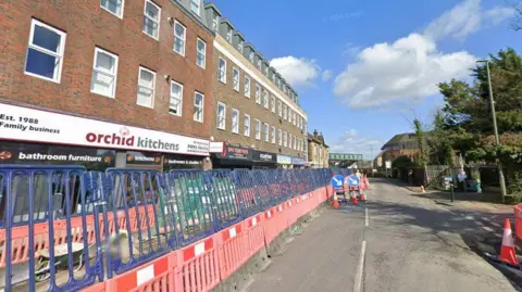 The image shows a high street where there are road barriers up blocking the road.