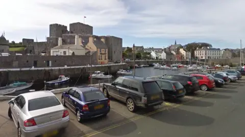 Castletown Harbour, with Castle Rushen in the background and a row of cars cars in the foreground.