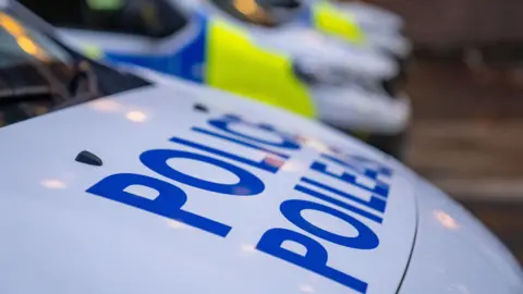 A Police Scotland van parked at the side of a road. It has blue and florescent yellow markings on the side, and a large blue Police Scotland logo