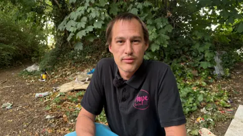Ben Schofield/BBC Pablo Tennant, sitting down, wearing a black T-shirt, sitting by foliage, that is behind him. He has short hair. 