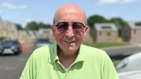 Glen Edwards, who is bald and wearing sunglasses, and is wearing a lime green T-shirt in a housing estate.