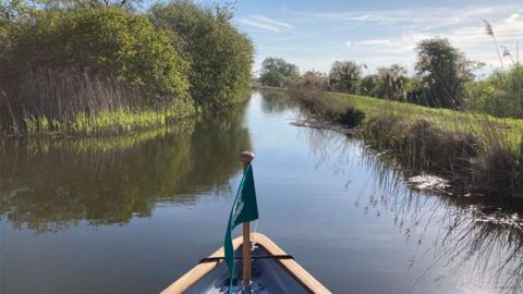 The prow of a boat with a National Trust flag on a river at Wicken Fen, Cambridgeshire 