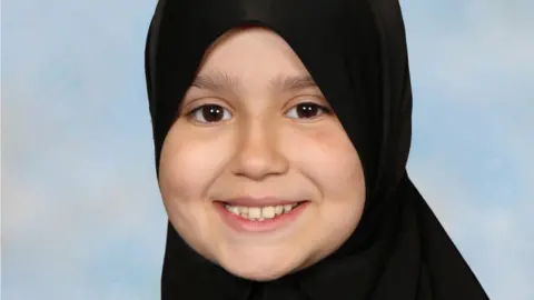 Surrey Police Sara Sharif smiling at the camera. She is wearing a hijab and looking directly at the camera.
