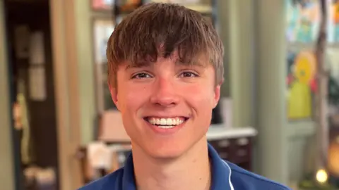 Barnaby Webber smiling at the camera. He is wearing a blue T-shirt