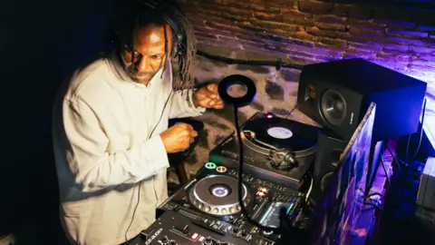 Martin Boileau A man is standing over turntables and DJ equipment