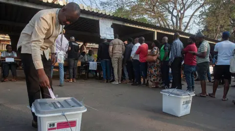 AFP via Getty Images to voter (fore) tosses its newsletter at the Election Department of the Civil Center in Lylongwe on September 16, 2025 during the presidential and parliamentary elections of Malawi. In the background, people are in line.