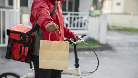 Witthaya Prasongsin / Getty Delivery cyclist holding food bag