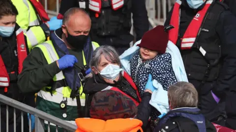 PA Media A young girl amongst a group of people thought to be migrants is carried by a Border Force officer as they are brought in to Dover