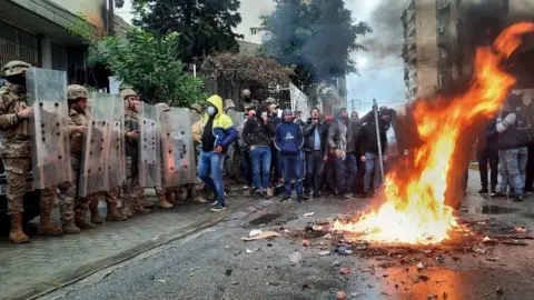 Reuters Security forces stand guard as demonstrators set fire near a politician's house in Tripoli, Lebanon. Photo: 28 January 2021