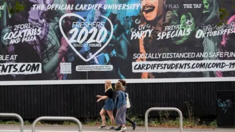 Getty Images Young women walking next to university poster