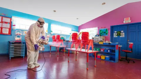 Getty Images A person in a biomass suit sprays a classroom