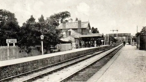 Public domain Black and white postcard showing railway line and station buildings