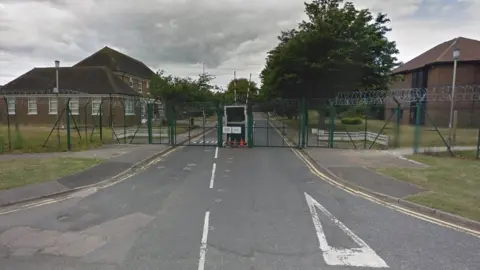 High green fencing and electronic gates with brick built buildings in the background which make up Howe Barracks