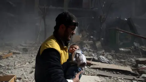 Reuters Amid rubble and smoke, a man wearing a headlamp and yellow jacket carries a baby in distress