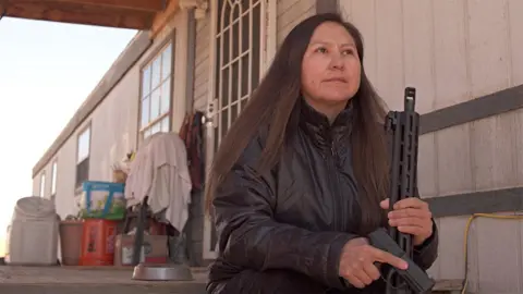 BBC Shiprock resident Bea Redfeather sits on her porch holding guns she bought to protect her family