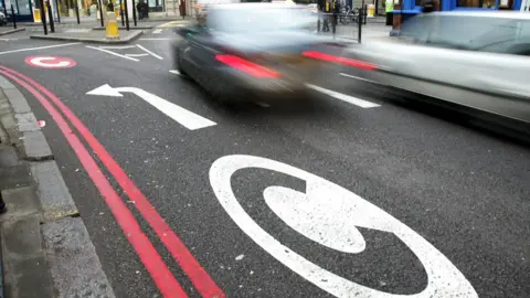 Associated Press Cars drive pass congestion charge signs