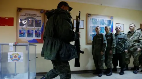 Reuters Armed soldier walks past ballot box as people line up to vote