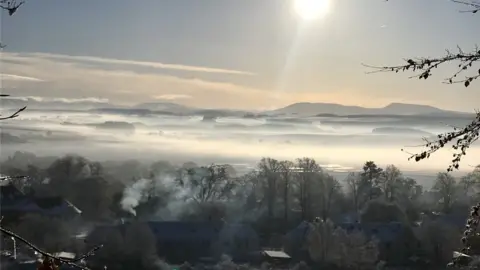 Joanne Jones Snow covered trees and buildings, mountains in the background