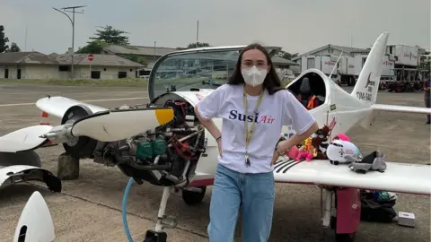 FlyZolo Zara Rutherford in Jakarta standing in front of her aircraft which has the nose cone and cowling removed.