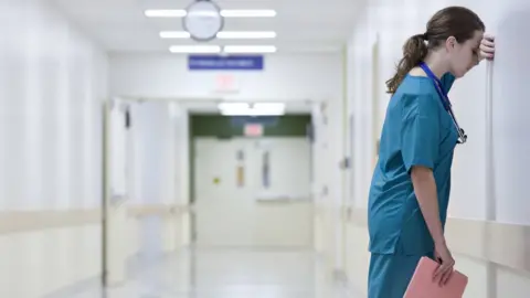 Getty Images upset doctor in corridor leaning with forehead to wall