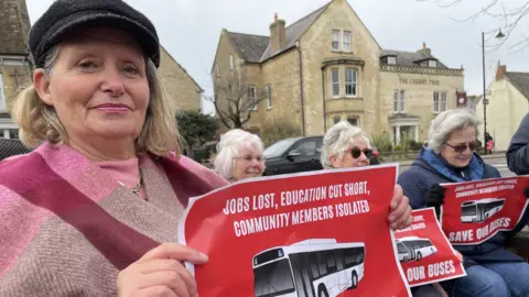 BBC Debbie Whitworth, Olney Town Council's deputy mayor, holding a poster denouncing the bus service reduction