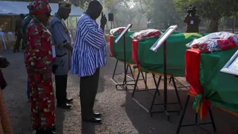 Reuters A relative of the former leader and revolutionary Thomas Sankara’s companion pays respects while standing by flag-draped coffins of Sankara and his companions before the burial of their remains in Ouagadougou, Burkina Faso February 23, 2023