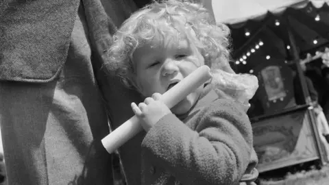 Historic England/John Laing Collection Child licks large stick of rock