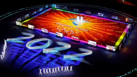 Reuters Figures gather around a giant projected logo of the Beijing 2022 Olympics