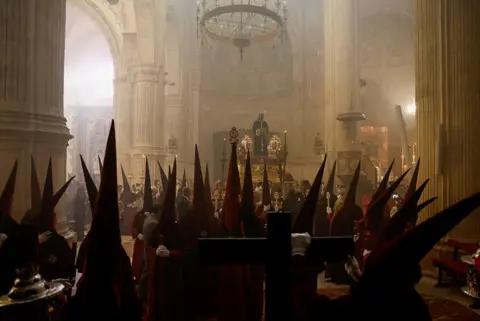 Jon Nazca / Reuters Penitents belonging to Los Gitanos brotherhood wait inside a church in Ronda