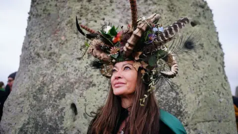 Ben Birchall/PA Woman in headdress looking up, in front of a stone at Stonehenge