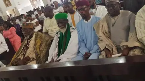 Sadiq Abdulai Abu Sheikh Osman Sharubutu (C), in green, sitting in a pew at the Christ the King Catholic Church in Accra, Ghana