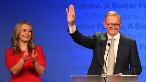 Getty Images Anthony Albanese waves from behind a lectern beside his partner