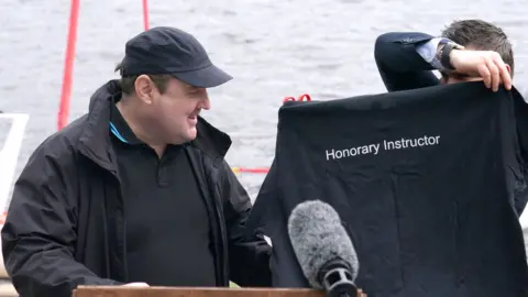 PA Media Peter Kay is given a shirt with the words Honorary Instructor on it