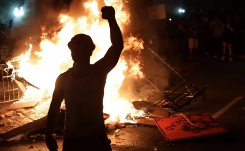 Getty Images A protesters stands by a fire near the White House in Washington DC. Photo: 31 May 2020