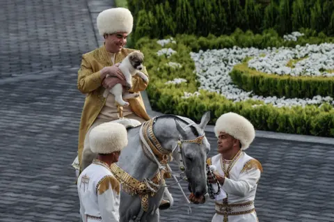 Getty Images President Berdymukhamedov on a horse holding a puppy
