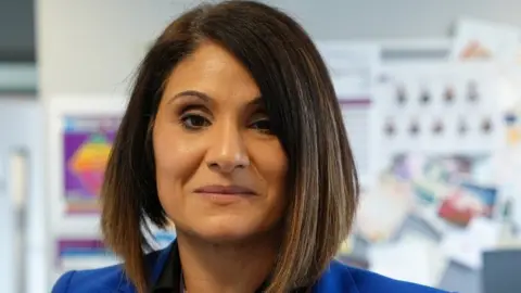 Nicola Haseler/BBC Rhoda McPherson smiling at the camera, appearing with brown hair and a blue jacket