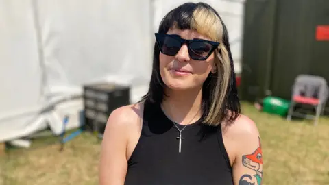 Creeper keyboardist and vocalist Hannah Greenwood smiling for the camera. She is wearing sunglasses and has a black vest on with a tattoo of a fox on her left arm