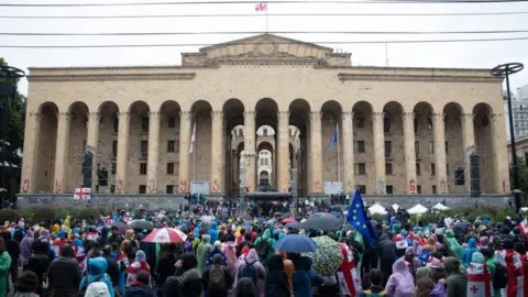 Getty Images Dozens of protesters waving flags and standing outside the Georgian parliament