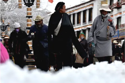 Getty Images People walk on the Barkhor street after a snowfall on December 8, 2023 in Lhasa, Tibet Autonomous Region of China.