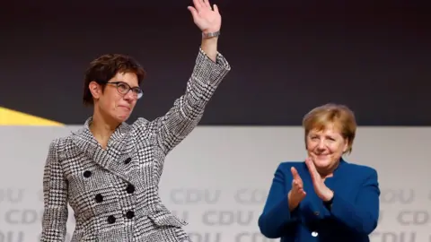 Reuters Annegret Kramp-Karrenbauer waves next to German Chancellor Angela Merkel after being elected as the party leader